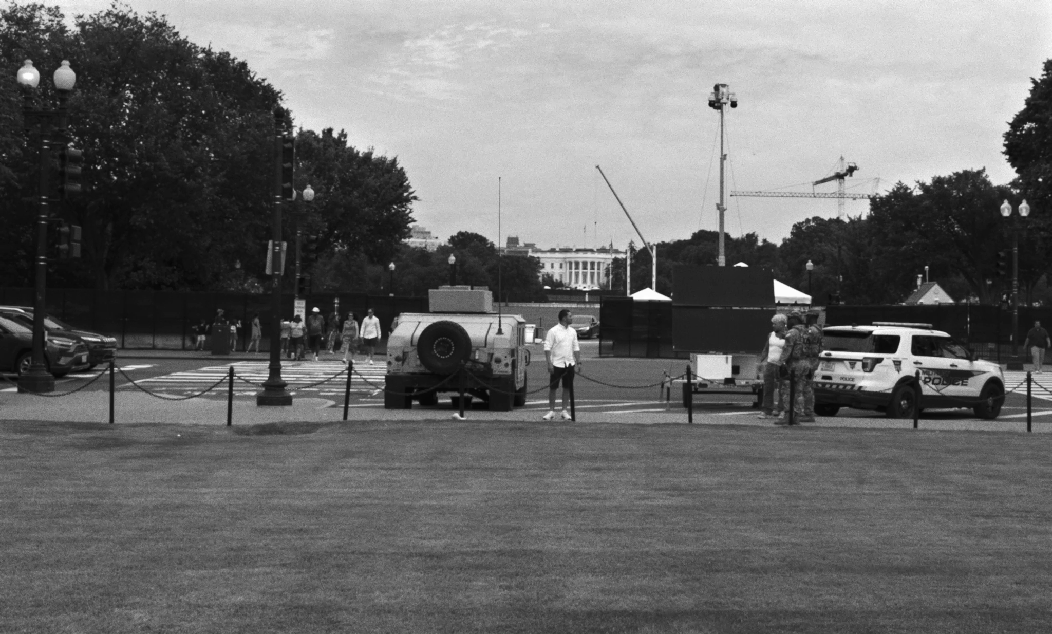 A man poses for a camera in front of the fortified White House, with the black fence in the middle ground